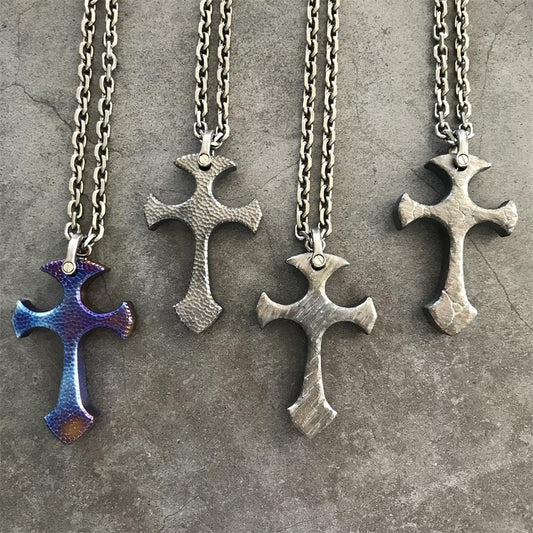 Four handmade titanium cross pendants in Blaze, Titan, Relic and Obsidian finishes lying side by side